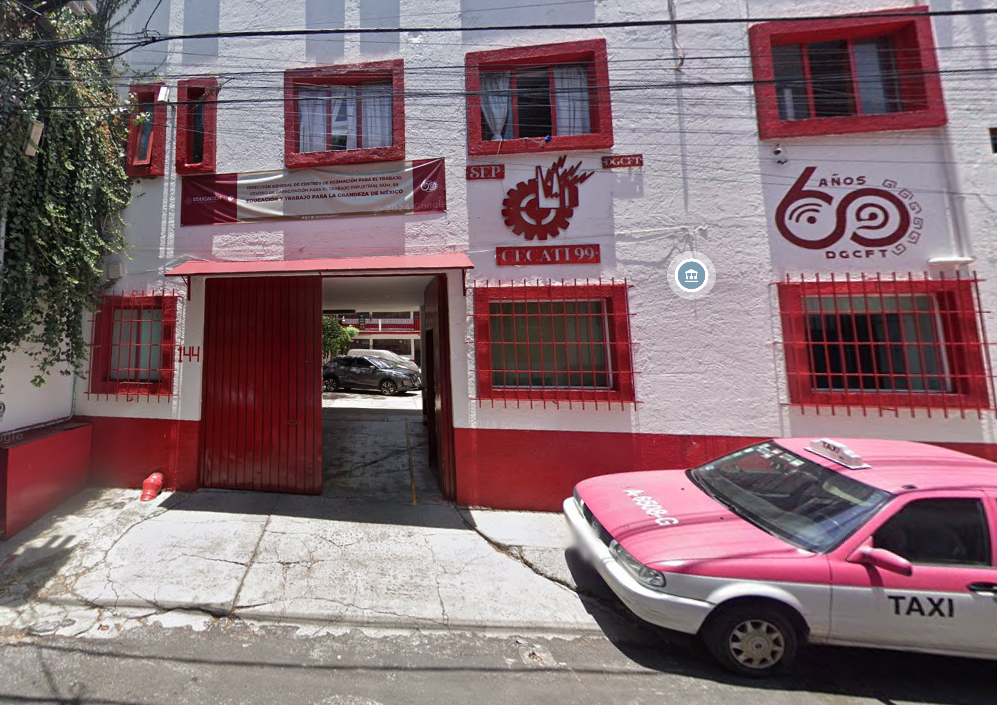 Fotografía en la que se muestra la fachada del plantel, que está conformada por un edificio de color blanco con ventanas rojas, sobre una de las ventanas dice CECATI 99. En la parte inferior del edificio hay un portón de color rojo que da acceso al plantel. Al lado izquierdo del portón está el número 144.
